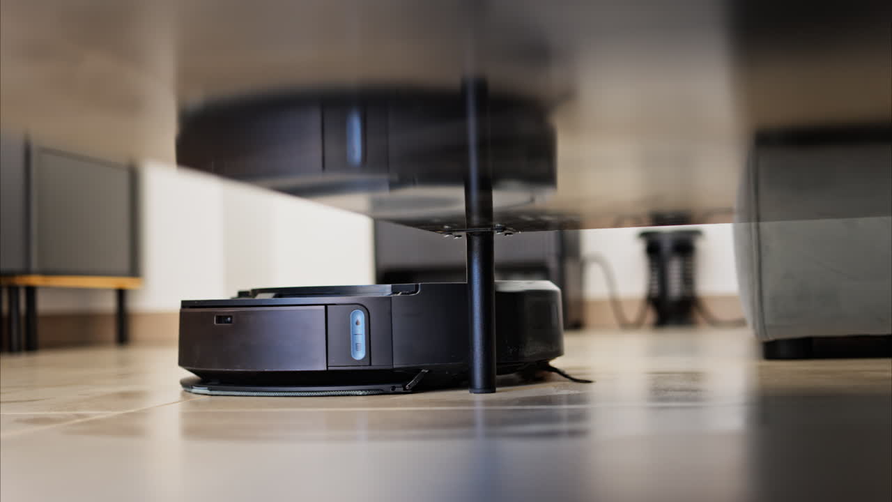 Close up of a small, black robot vacuum cleaning under surfaces in the house