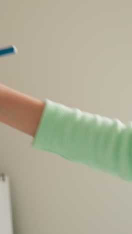 cute little girl takes off cap from blue felt-tip pen and stretches out hand writing or drawing on board slow motion. serious schoolkid does schoolwork in light room closeup