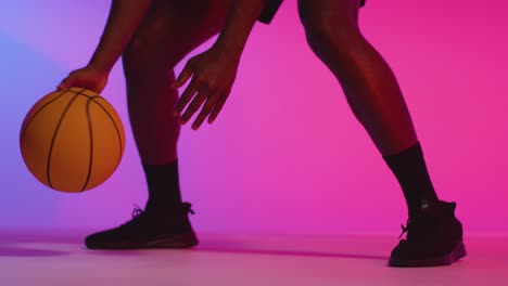 close up studio portrait of male basketball player dribbling and bouncing ball against pink lit background 7