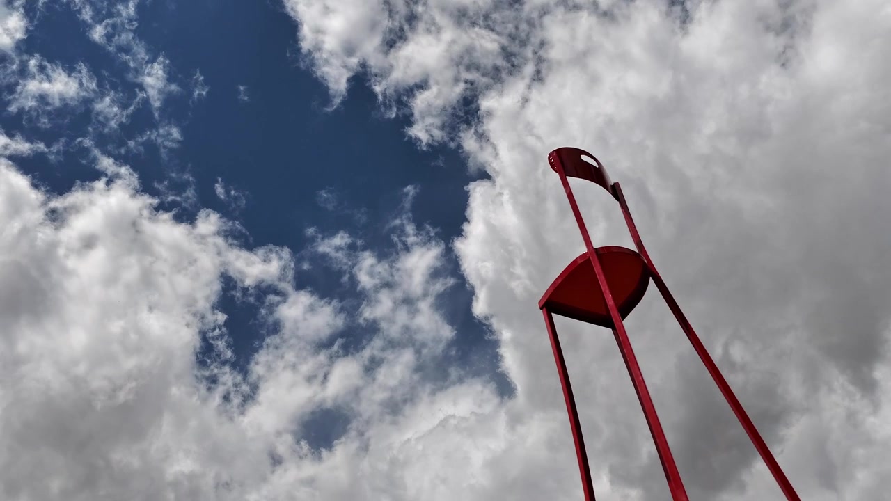 Een surrealistische, grillige timelapse legt een lange rode stoel vast die omhoogkijkt naar snelbewegende wolken. Deze conceptuele en metaforische B-roll biedt een unieke opening of overgang voor fantasy-verhalen.