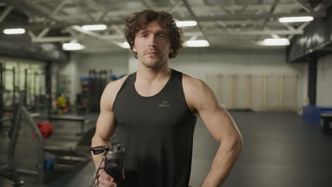 portrait of muscular man holding water bottle in gym