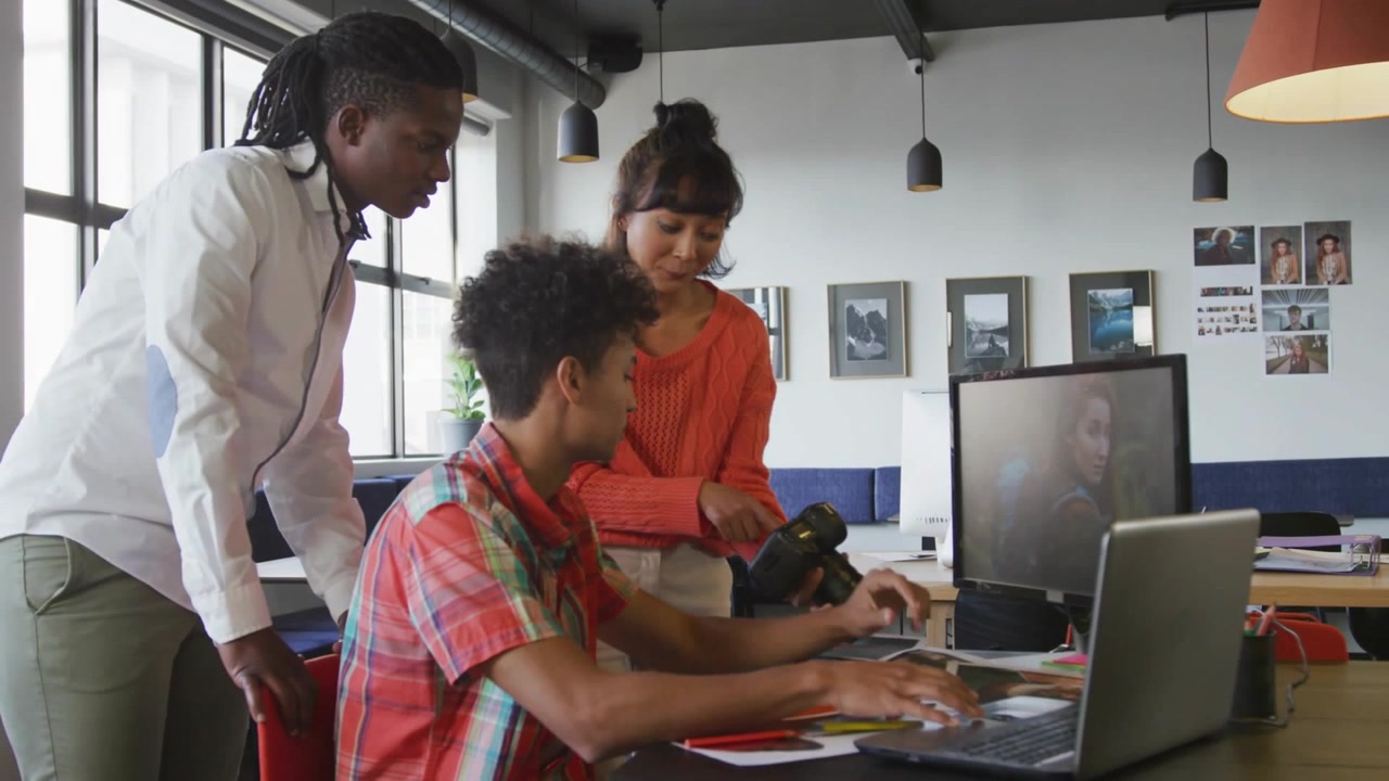 Seated creator tapping laptop and activating social notifications, team reacting and editing camera