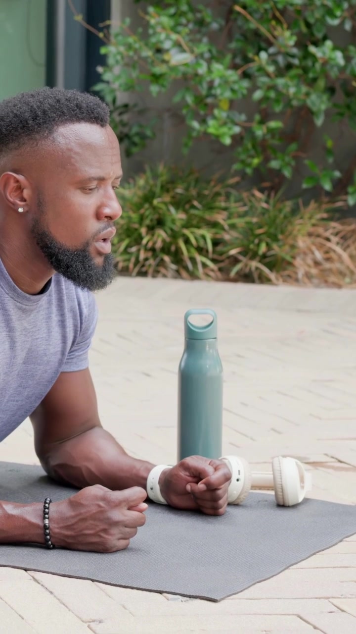 Vertical video: Starting man in tee plank shifting to side plank on patio for core glancing bottle