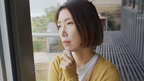 asian woman wearing jumper thinking and touching her chin on balcony