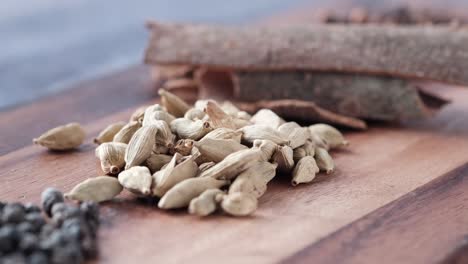 cardamom, cinnamon, and peppercorns on a wooden cutting board