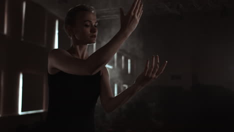 prima ballet company in a dark dress on a dark theater stage rehearsing in the smoke performs dance moves in slow motion.