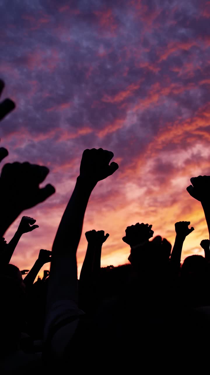 Silhouetted fists raised against a vibrant sunset sky, captured from a low angle
