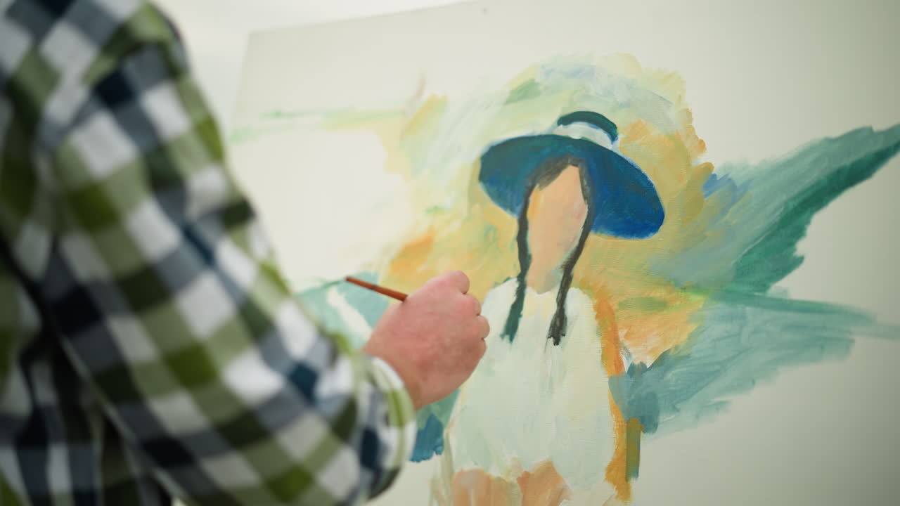 художник, одетый в шариковую рубашку и шляпу, тщательно создает яркий портрет на холсте. близкий кадр подчеркивает тщательные штрихи и сосредоточенность художника на произведении искусства