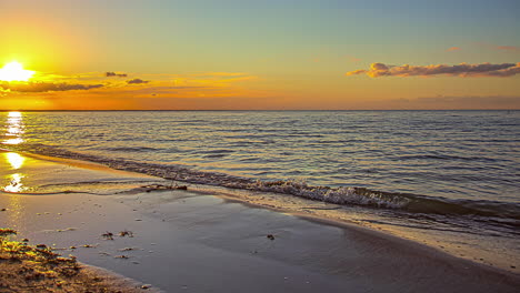 waving water of ocean reaching sandy beach and reflecting by golden sun during sunset at horizon,time lapse