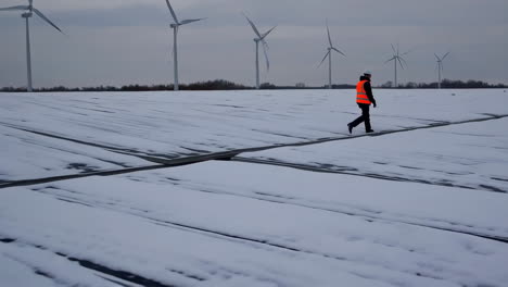 engineer walks across a snow-covered field with wind turbines in the background