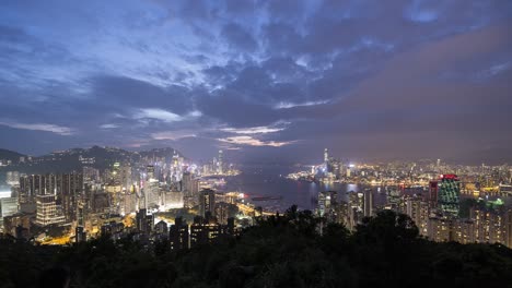 beautiful timelapse of hong kong city skyline, victoria harbor during sunset with bright city lights turning on, ships and boats moving in harbor and thick clouds flowing