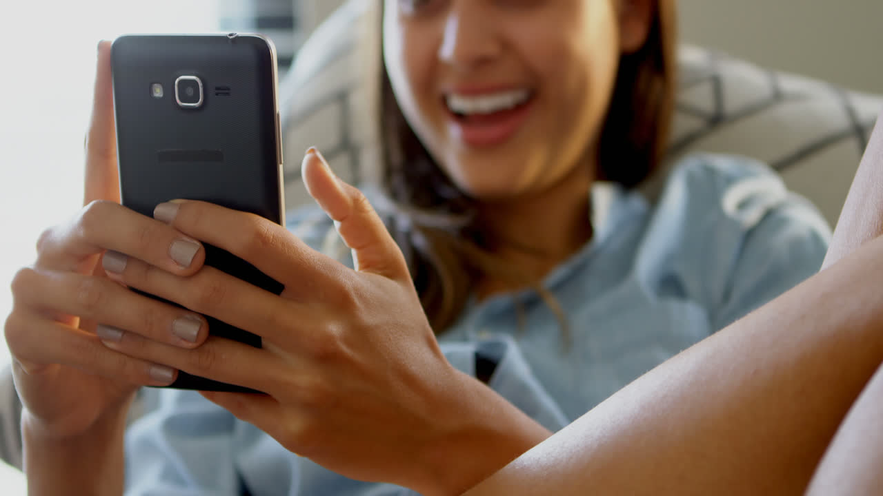 거실 4k의 소파에서 휴대 전화를 사용하는 웃는 여성