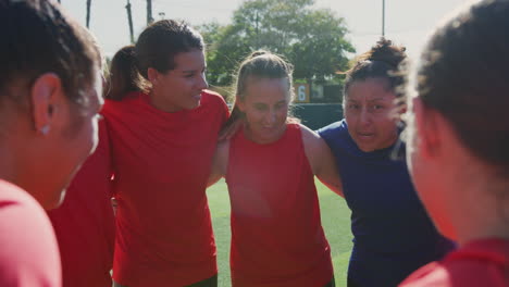 manager joining hands with womens soccer team during motivational pep talk before match