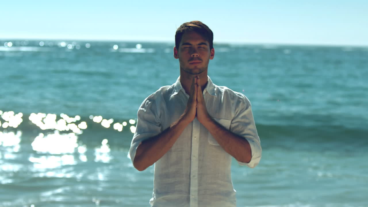 Handsome man practicing yoga on the beach