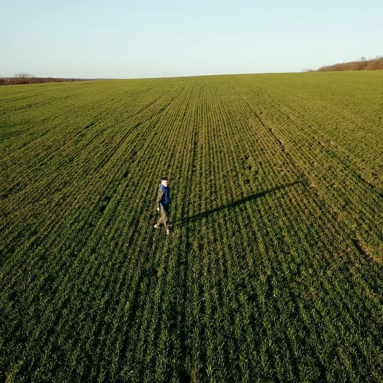 Cute boy running and turning around on the spacious green field in spring. Little kid in sportsuit playing outdoors on the natural background. Aerial view