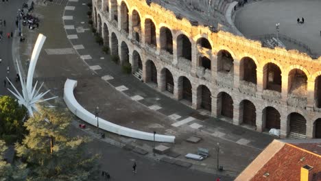 Toma-Aérea-Cercana-De-Un-Dron-De-La-Fachada-De-La-Arena-De-Verona,-Con-Gente-Lejana-En-La-Plaza,-Sin-Clasificar