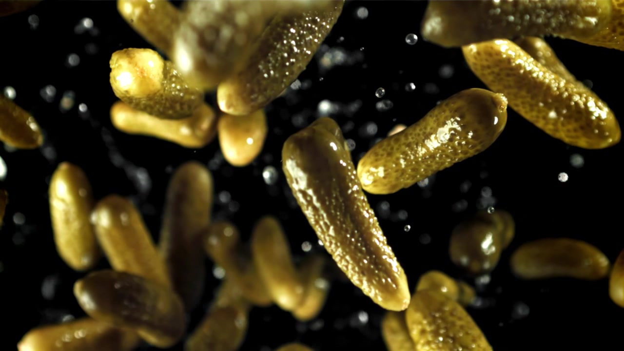 Cetriolini sottaceto che cadono al rallentatore con gocce d'acqua