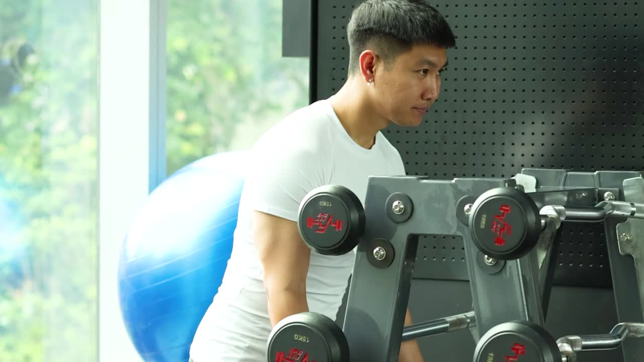 A fit man in a white shirt chooses weights from a rack for his workout