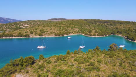 Yachts-dock-in-a-bay-near-the-coastal-city-of-Croatia-against-a-backdrop-of-blue-skies-and-blue-clear-water,-green-lush-trees-and-houses-with-red-roofs