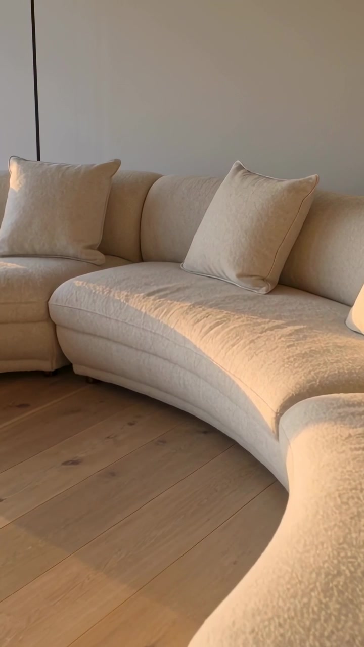 Vertikal video: Panorerende kamera viser buet cremefarvet sofa i stue, fremhæver to puder