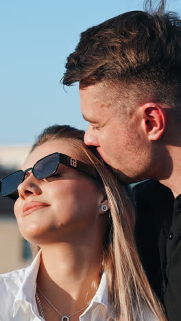 upper part of a couple standing outdoors in the sun. man kisses his woman wearing sunglasses. vertical video
