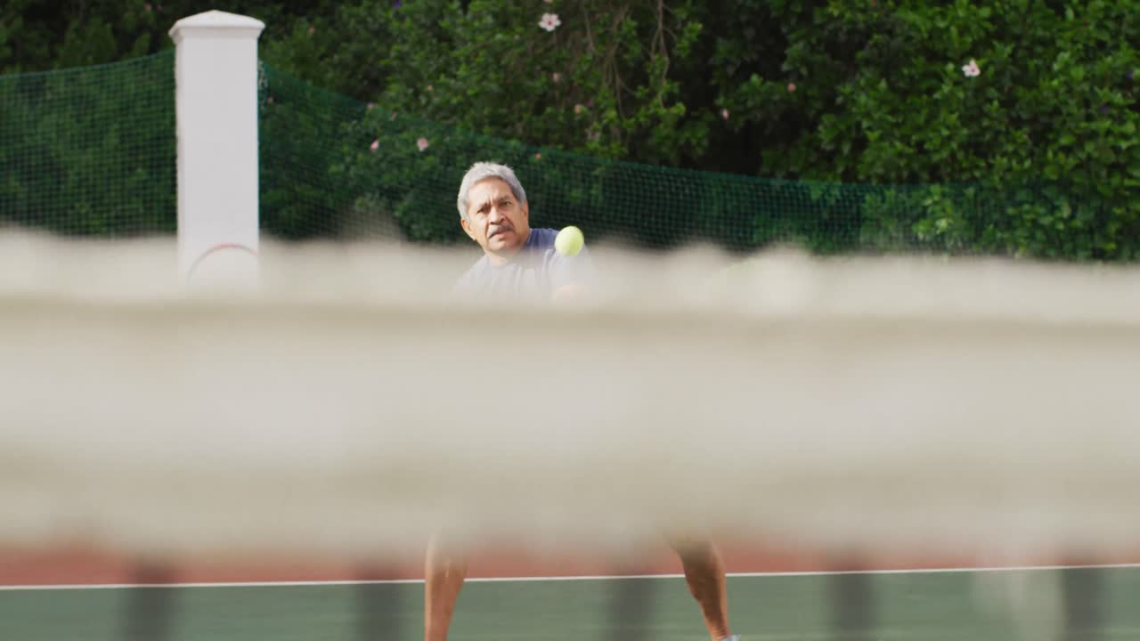 테니스 코트에서 테니스를 하는 두 인종의 노인 남자에 초점을 맞춘 비디오