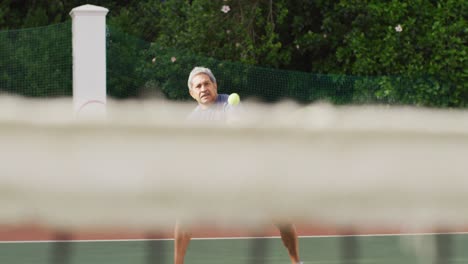 video of focused of biracial senior man playing tennis on tennis court