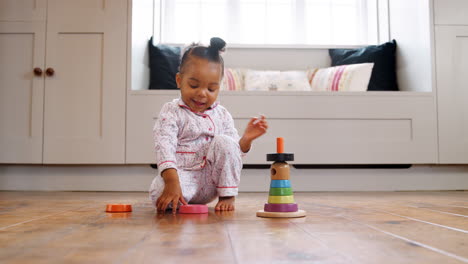 smiling female toddler at home playing with wooden stacking toy