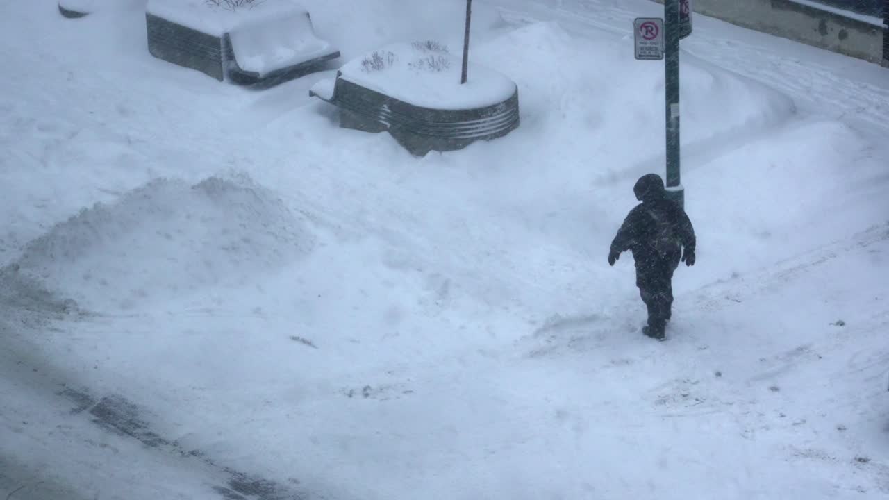 코트와 배낭을 입은 외로운 사람이 낮 4k 동안 추운 폭풍 도시 눈 덮인 거리를 걷습니다.