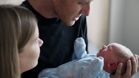 father waving a tiny newborn trying to calm his cry. mother stands beside looking at her baby boy. close up.