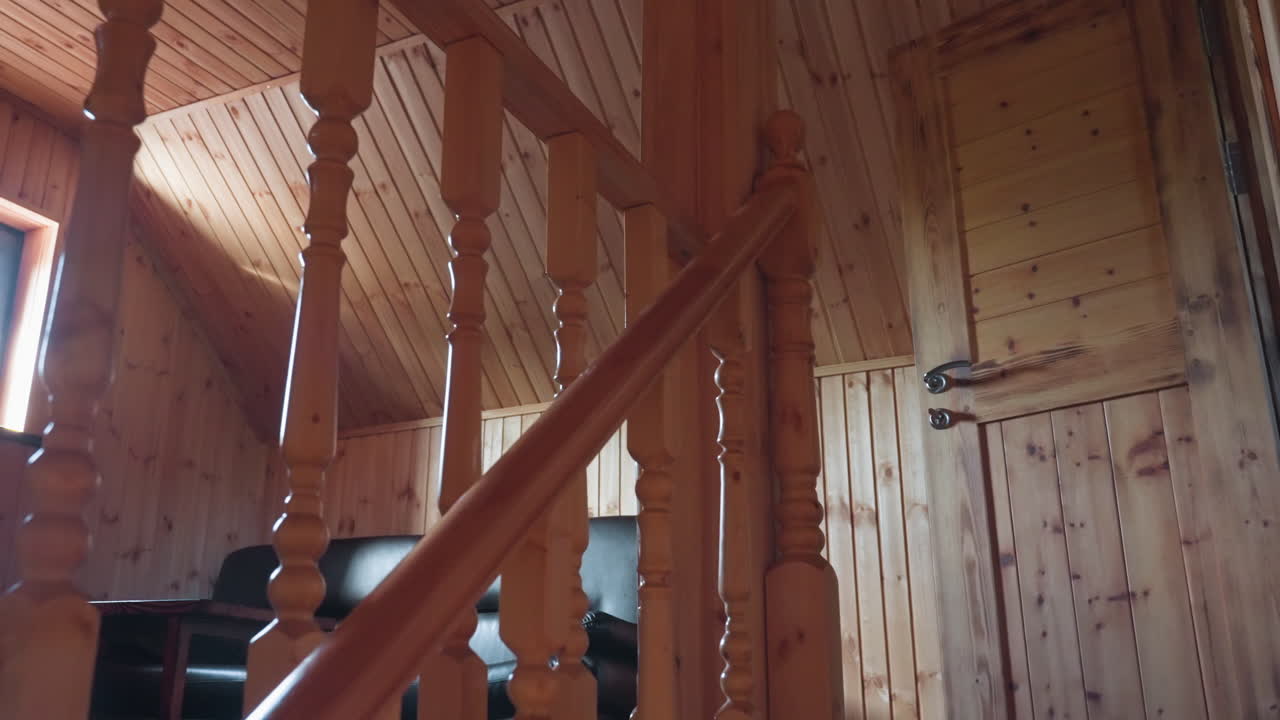 Wooden staircase ascending toward rustic wooden door with visible leather chair positioned at top landing, featuring polished wood panel walls, carved railing