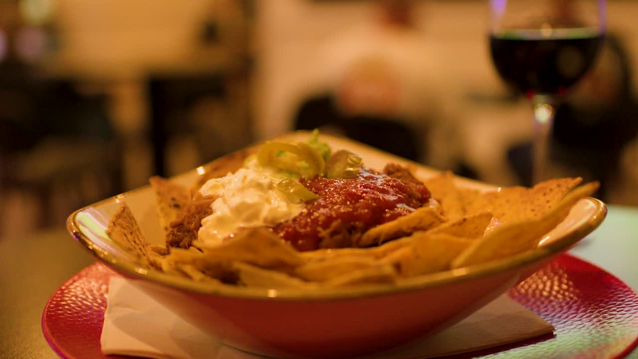 Close-up of hand dipping tortilla chip into nachos with salsa, cheese, and sour cream