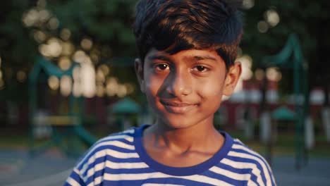 young boy radiating genuine happiness while standing in sunlit park during golden hour, warm natural background highlighting childhood innocence and carefree joy