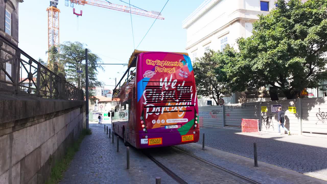 A colorful double-decker tour bus drives through a sunny street in Porto, Portugal