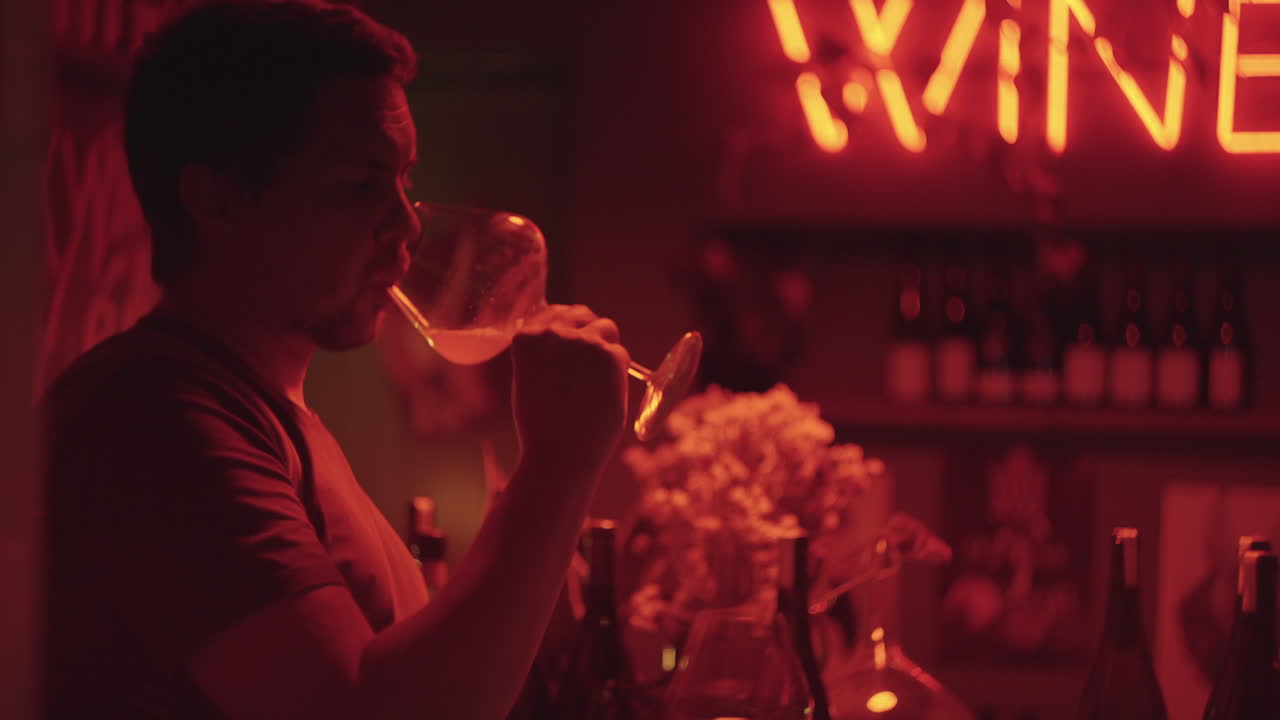 은 빛 으로 조명 된 와인 바 에서 와인 을 마시는 사람