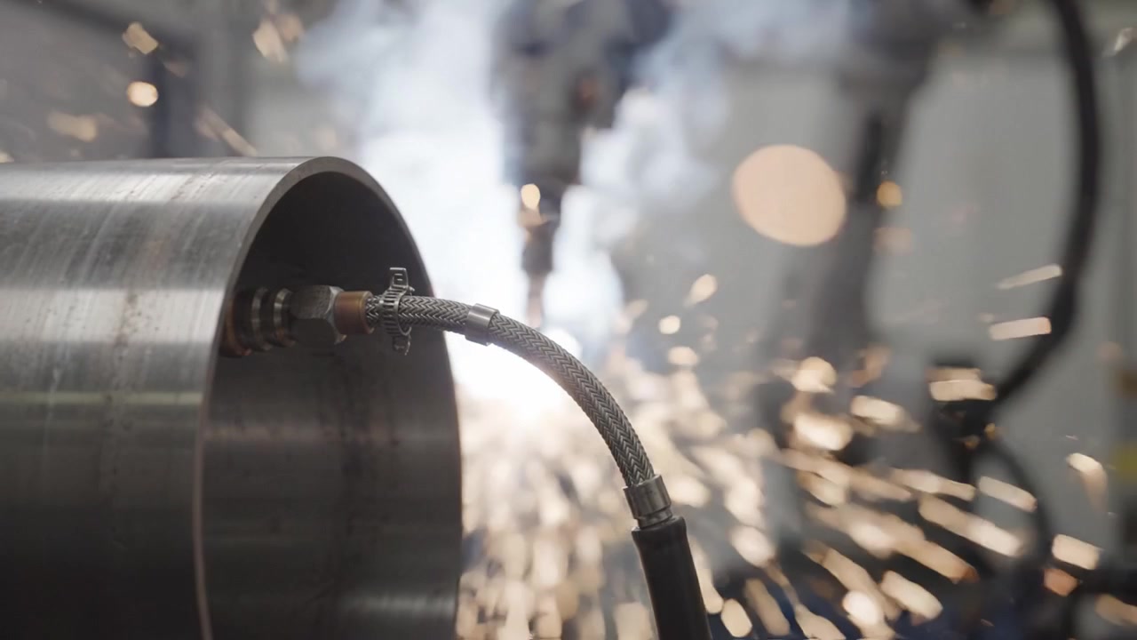Robotica industriale: processo di saldatura di precisione con scintille e fumo emessi da un cilindro d'acciaio in un ambiente di produzione automatizzato.