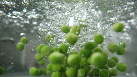 underwater macro view of green peas falling into a pot of boiling water for soup, macro and slow motion