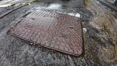burst drain cover with treated water pouring out into street. leaking liquid in need of repair maintenance from water company professional plumber repairman. wide angle.