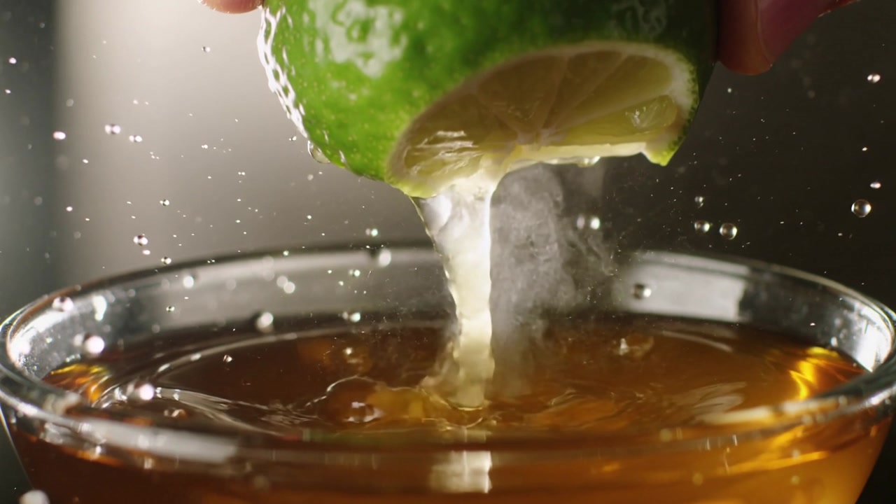 Pressing hand squeezing halved lime over studio glass, juice streaming, steam rising, flavoring tea