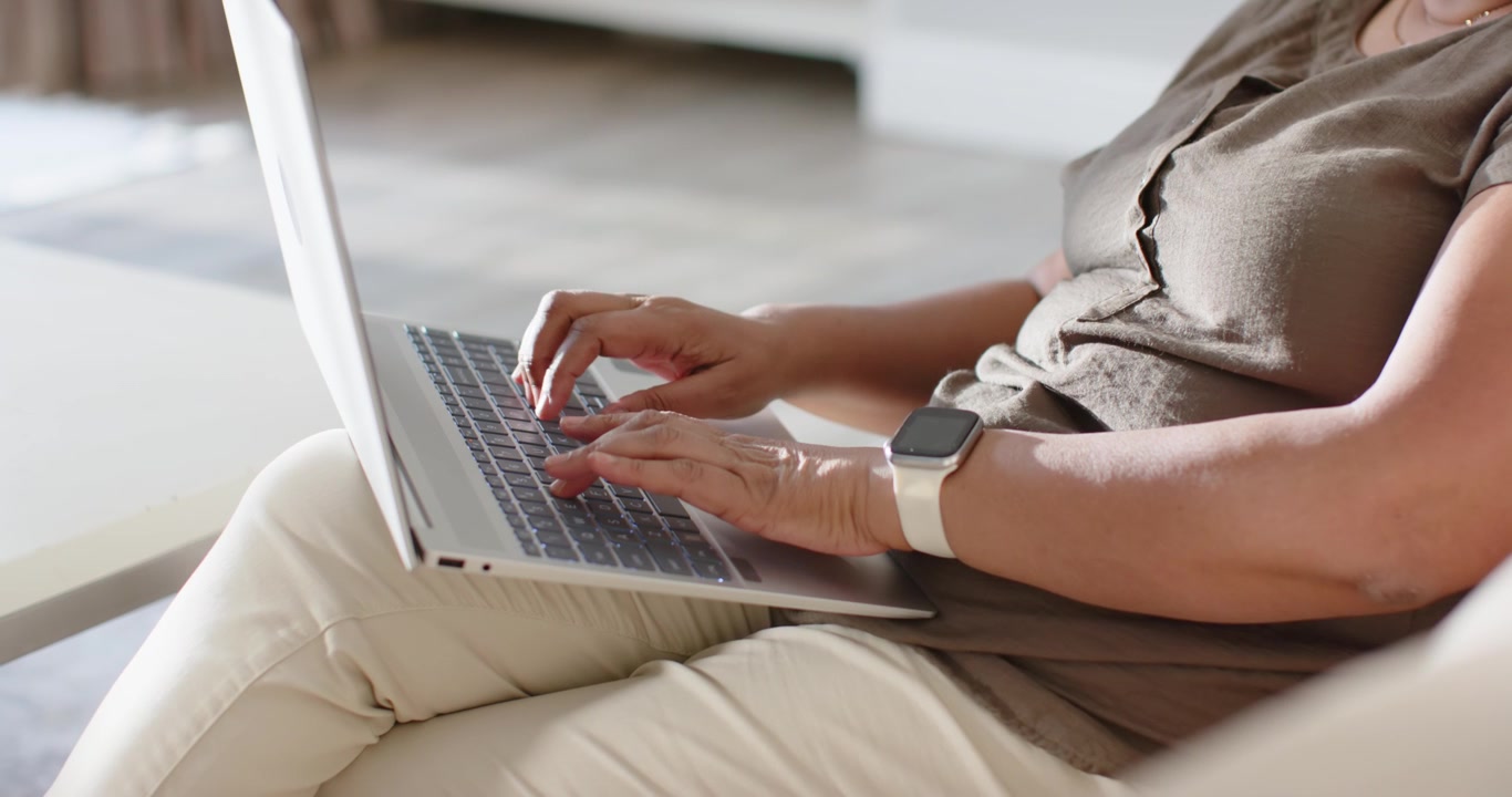 African American woman starting with hands poised, typing on silver laptop on sofa, finishing work