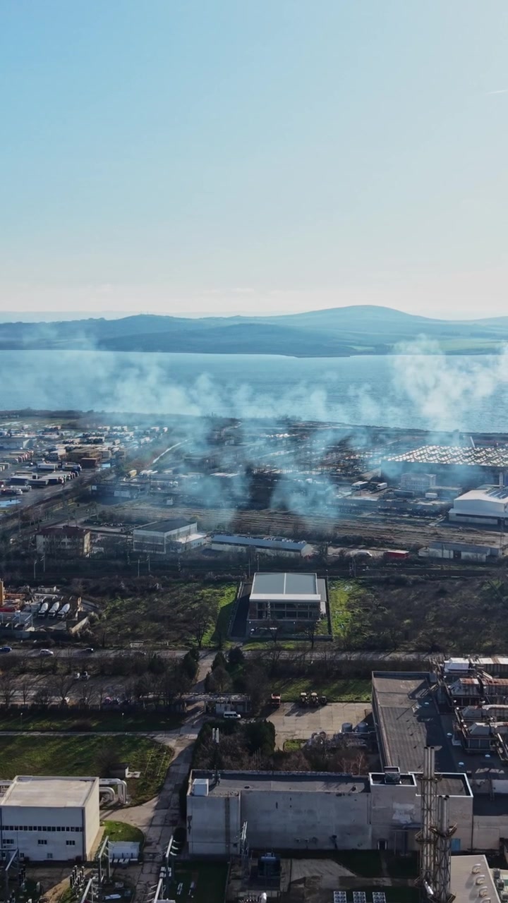 Factory near water with smoke rising in the background during the day