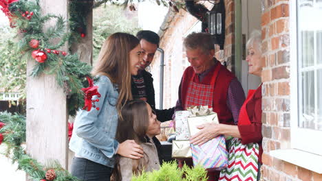 family being greeted by grandparents as they arrive for visit on christmas day with gifts