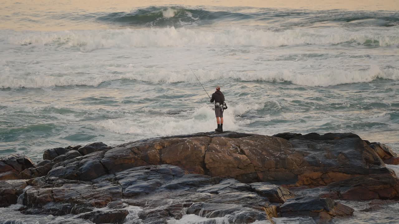pescador pescando en agua salada desde rocas con olas rompiendo cerca