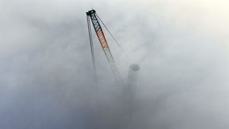 tall smokestack shrouded in dense gray fog, visible between dense clouds of construction tower project, high aerial perspective