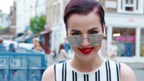 mujer elegante con gafas de sol de pie fuera del edificio de la ciudad