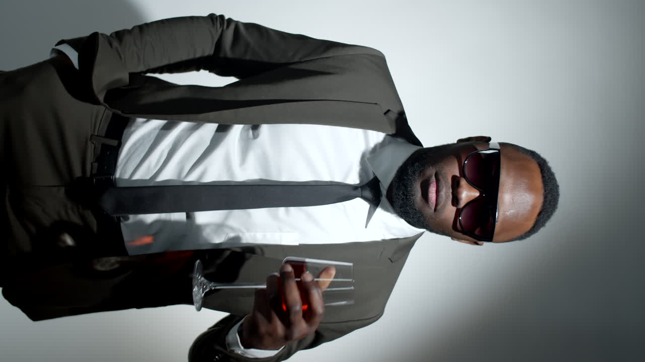 패션 흑인 남자가 스튜디오에서 와인과 포즈를 취하고 있습니다.