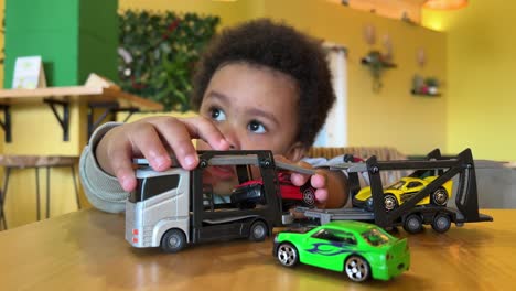 Two-year-old-black-baby,-mix-raced,-playing-with-his-toy-truck-and-cars-and-eating-a-croissant-in-a-cafeteria