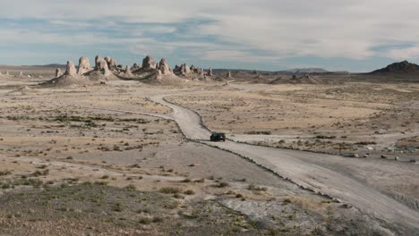 a car is driving in the desert in back are stunning rock formations