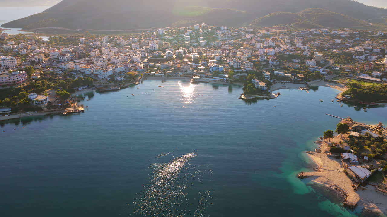 Aerial drone view of Ksamil town, it's dense cluster of hotels and houses, and the iconic bright blue bays with floating platforms and beach clubs