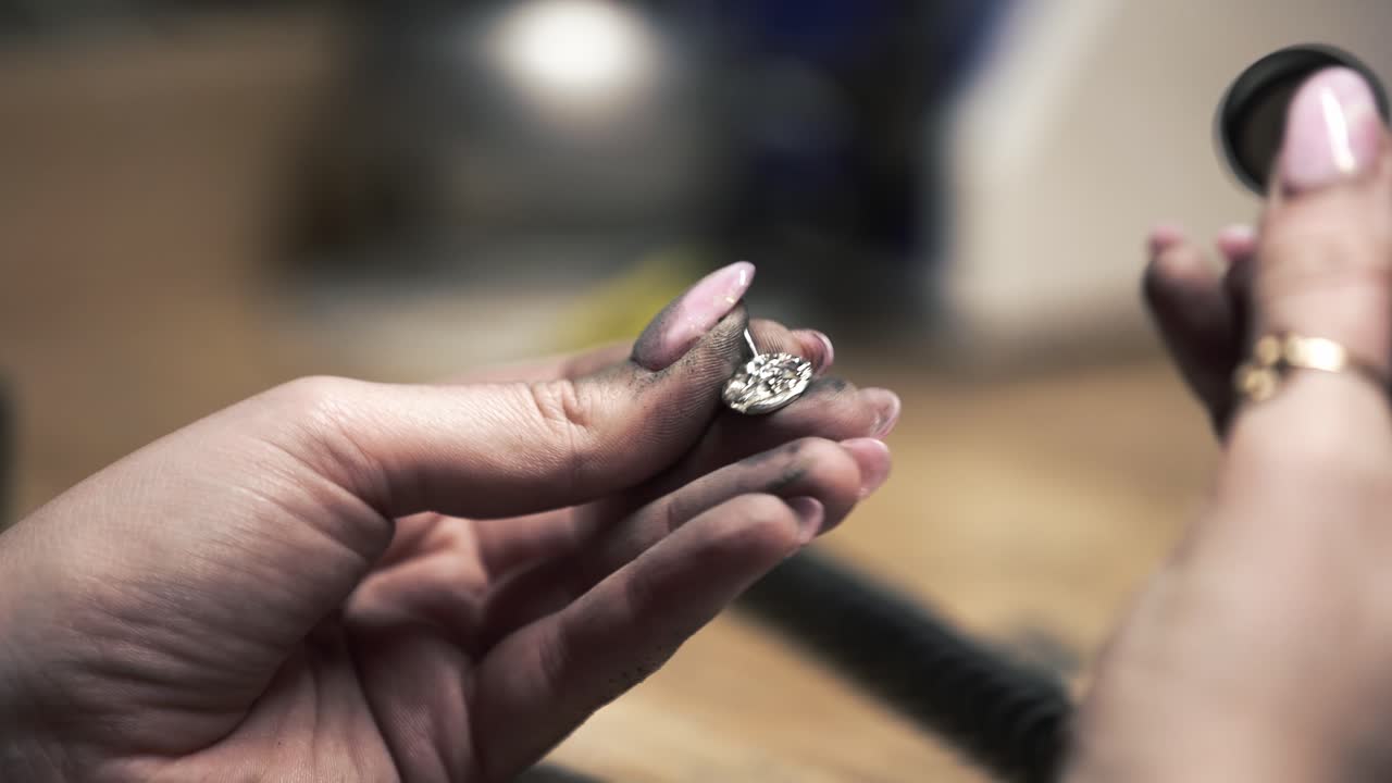 fotografía de cerca de una joyería metalúrgica femenina usando una máquina de lijar para pulir un collar de metal plateado